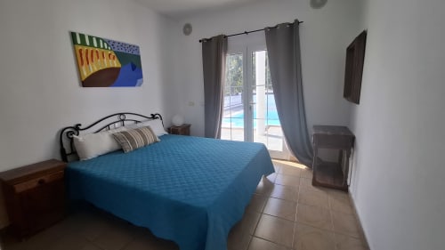 Bright bedroom in Puerto Calero villa with blue bedspread, wrought iron headboard, terrace doors overlooking pool, and