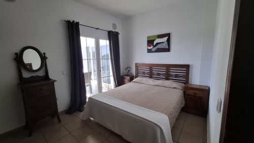 Spacious bedroom in Villa 1 at Villas del Mar, Puerto Calero, with wooden bed, dark curtains, and balcony access with sea