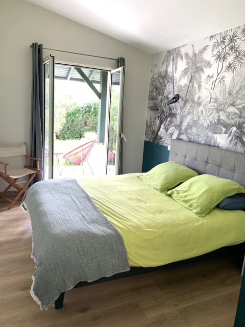 Chambre moderne avec literie vert citron, fresque jungle, tête de lit capitonnée grise et portes-fenêtres sur vue montagne