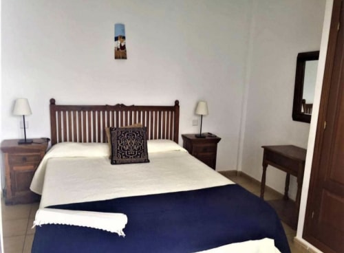 Bedroom in Villa 8 at Villas del Mar with wooden bed frame, white bedding, dark blue throw, and dark wood nightstands with