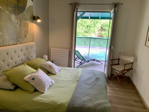 Chambre lumineuse de la Villa Ongizatea avec vue sur la piscine par les portes de la terrasse, linge de lit citron vert, tête de lit crème et bois