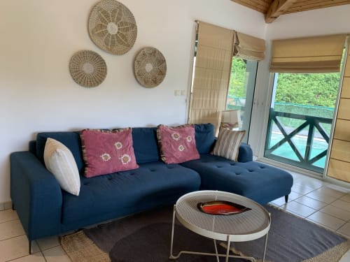Modern living room with navy sectional sofa, burgundy pillows, woven wall decals, and glass doors opening to pool terrace at