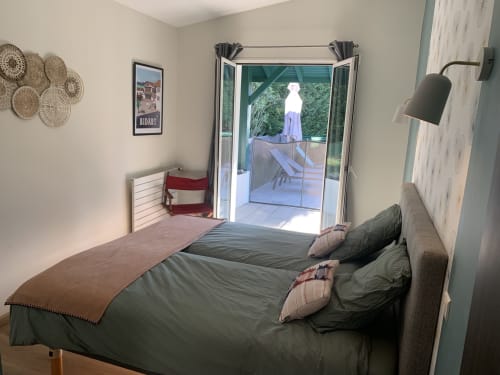 Chambre lumineuse à la Villa Ongizatea avec literie verte, portes donnant sur la terrasse avec vue piscine à Urrugne