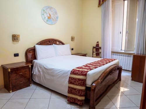 Camera elegante presso Alla Basilica Rooms a San Giovanni con letto in legno, biancheria bianca e pareti color crema
