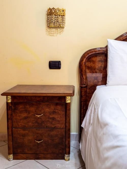 Camera elegante di Alla Basilica Rooms con comodino in legno, biancheria bianca e applique dorato a San Giovanni