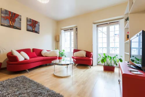 Sala de estar moderna e luminosa em Heart Pulse Stays Lisboa, com sofá vermelho, poltrona, mesa de centro em vidro e portas para a varanda