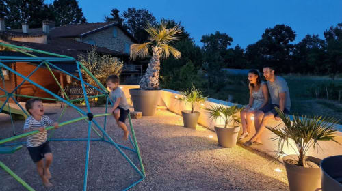 Famille profitant de la soirée au gîte Le Clos Des Anges à Bagnols avec structure de jeux et plantes tropicales