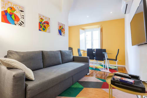Sala de estar moderna no Lisbon Heart Pulse Stays com sofá cinzento, parede de destaque amarela, arte colorida e tapete geométrico.