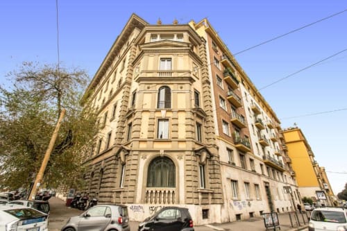 Suggestivo palazzo beige d'epoca a Roma, angolo con architettura ornamentale, balconi e auto parcheggiate sotto cielo limpido
