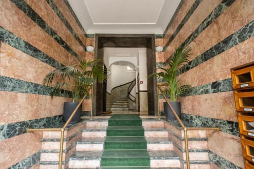 Elegante ingresso con scala in marmo presso l'appartamento Downtown Srl Roma, con pareti a righe verde e terracotta, ringhiere e