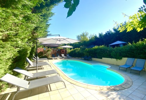 Piscine turquoise avec transats et parasols, entourée de haies verdoyantes à la villa Ô Clair De Lune à Sarlat, France