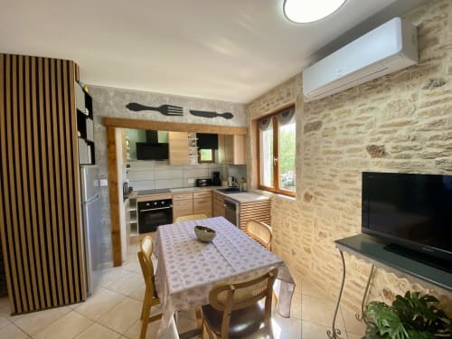 Cuisine-salle à manger de cottage moderne avec murs en pierre, meubles en bois, climatisation, TV et table à manger à Ô Clair De