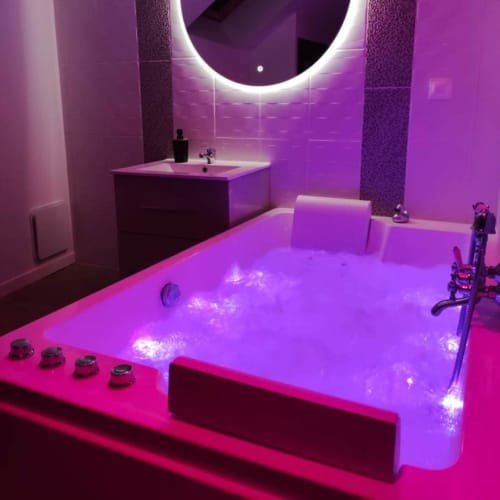 Salle de bains luxueuse à LA MAISON DEFENDUE avec éclairage LED néon violet, baignoire illuminée, vasque et équipements modernes
