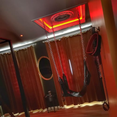 Chambre néon rouge avec chaînes et équipements intimes à La Maison Defendue à Tessy-Bocage