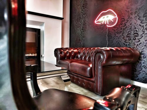 Canapé Chesterfield bordeaux dans le salon d'un appartement moderne avec enseigne néon lèvres, papier peint damassé et cheminée à La Maison