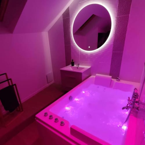 Salle de bain moderne rose néon à La Maison Defendue avec miroir rond illuminé, baignoire et lavabo