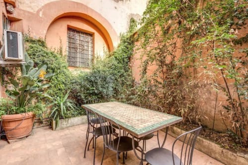 Area pranzo all'aperto dello Smart Loft a Roma con muri in terracotta, edera, tavolo e sedie
