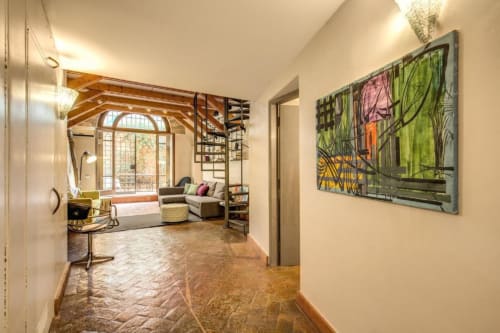 Il corridoio dell'appartamento Smart Loft a Roma con opere d'arte moderna, che conduce alla zona living con travi a vista e grandi finestre