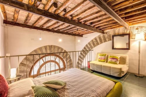 Camera da letto Smart Loft a Roma con travi di legno a vista, arcate in mattoni, letto matrimoniale e divano color crema in zona living