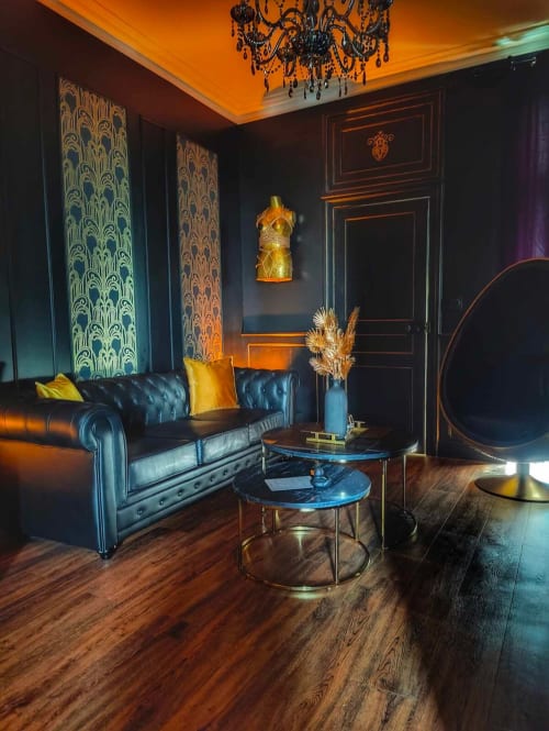 Salon luxueux de La Cage Dorée à La Maison Defendue, Tessy-Bocage, avec canapé en cuir noir, accents dorés et motifs raffinés