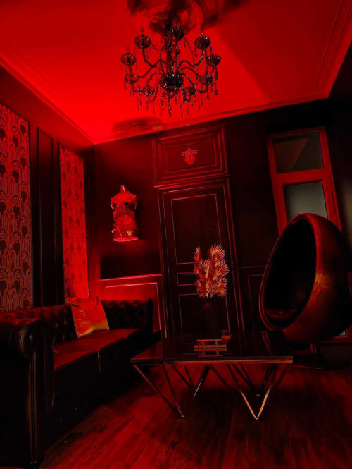 Salon dramatique aux lumières rouges à La Maison Defendue avec lustre, canapé, fauteuil rond et éléments décoratifs