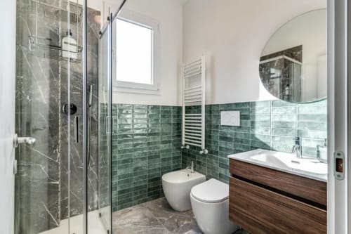 Bagno moderno con piastrelle verdi, doccia walk-in, mobile in legno e specchio rotondo in appartamento a Roma