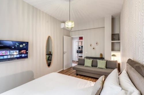 Camera da letto moderna in The Cloud, Downtown Srl Roma con letto, divano, TV, specchio ovale e pavimento in legno