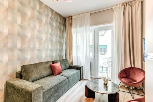 Moderno salotto dell'appartamento The Cloud con divano grigio, poltrona color corallo e accesso al balcone nel centro di Roma