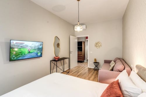 Camera da letto moderna con letto bianco, divano rosa, TV a schermo piatto, lampada a sospensione e pavimentazione in legno nel centro di Roma