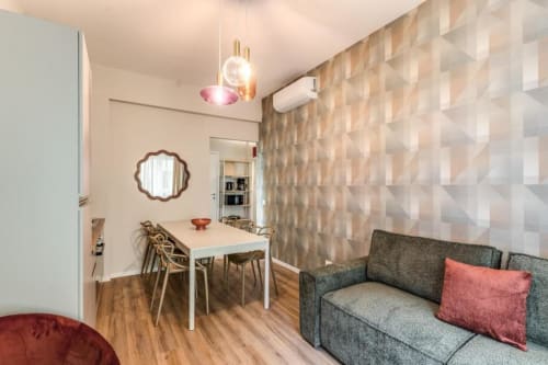 Moderna zona living con divano grigio, tavolo da pranzo, carta da parati geometrica e illuminazione a sospensione nel centro di Roma