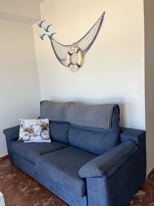 Estudio en apartamento costero con sofá azul, decoración náutica con red de pesca y salvavidas en Apartamentos A la Orilla