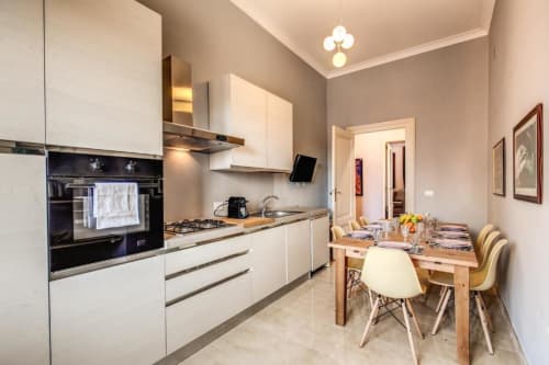 Cucina e zona pranzo moderna con mobili bianchi, forno nero, tavolo in legno e pareti beige a Roma.