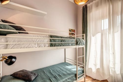 Letti a castello in metallo bianco con biancheria verde in camera da letto luminosa con luce naturale e arredi moderni