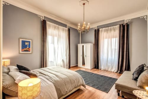 Elegante camera da letto nell'appartamento Retro di Roma, con letto matrimoniale, lampadario, finestre doppie con tende e arredamento moderno