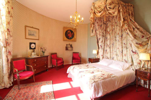 Elegant bedroom suite at Domaine de Bort near Limoges with canopy bed, red velvet chairs, and floral décor