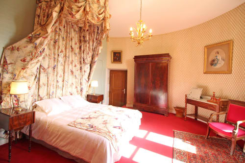 Chambre élégante au Domaine de Bort avec lit à baldaquin fleuri, mobilier d'époque, tapis rouge et papier peint pêche près de Limoges