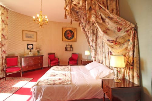 Luxury bedroom at Domaine de Bort near Limoges with canopy bed, red armchairs, floral curtains, and period furnishings