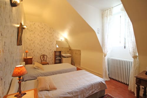 Cozy bedroom at Domaine de Bort near Limoges with twin beds, floral wallpaper, and sloped ceiling