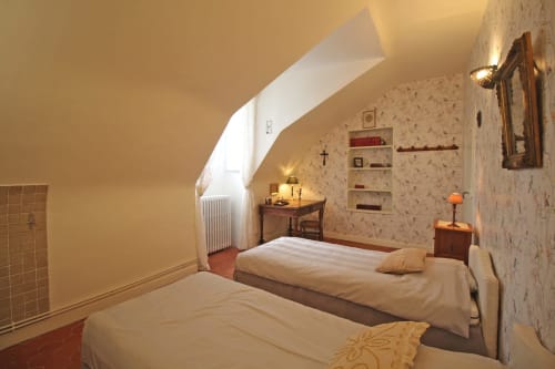 Cozy attic bedroom at Domaine de Bort with twin beds, period wallpaper, desk, wooden beams, and warm lighting