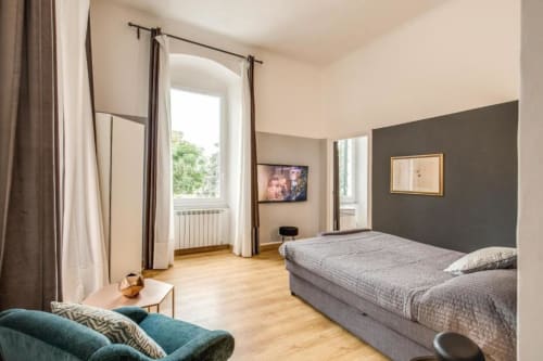 Camera da letto moderna con letto matrimoniale, divano teal, parete in accento scuro e grandi finestre con vista sul giardino nell'appartamento delle Cinque Terre