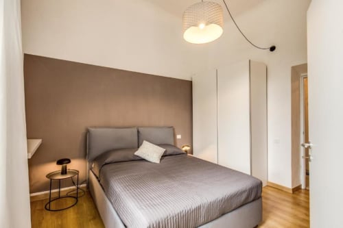 Camera da letto moderna in appartamento a Cinque Terre con biancheria grigia, parete in accento marrone, lampada a sospensione e pavimenti in legno
