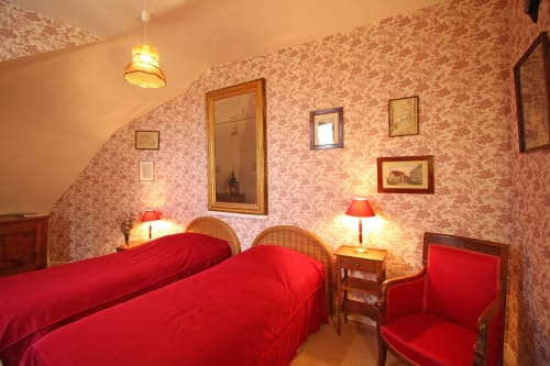 La Suite de la Tour bedroom at Domaine de Bort with twin beds, red bedding, floral wallpaper and antique furnishings near