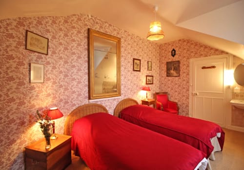 Elegant bedroom at Domaine de Bort with twin beds, red bedding, floral wallpaper, and warm lighting near Limoges