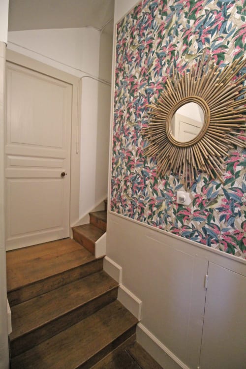 Elegant hallway at Domaine de Bort with floral wallpaper, sunburst mirror, wooden stairs, and white wainscoting