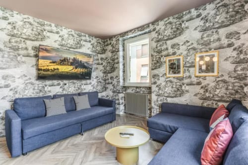 Soggiorno moderno nell'appartamento Cinque Terre Swing con divani blu, carta da parati in betulla, tavolo rotondo giallo e TV a muro