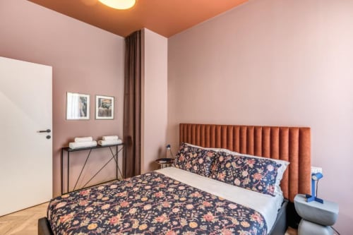 Camera moderna nell'appartamento Cinque Terre Swing con pareti rosa, letto a fiori e testata in terracotta.
