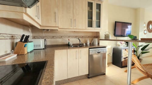 Moderna cocina con muebles de madera clara, encimeras de granito y electrodomésticos de acero inoxidable en apartamento Bakit House, Águilas