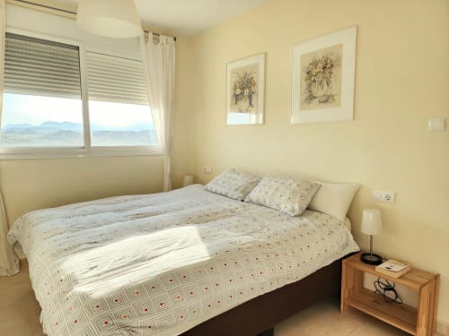 Dormitorio luminoso en BAKIT HOUSE, Águilas, con vistas al mar, ropa de cama beige, mesita de noche de madera y vistas a la montaña