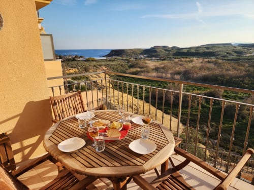 Mesa de comedor de madera en balcón soleado con vistas al Mar Mediterráneo y colinas costeras de BAKIT HOUSE, Águilas