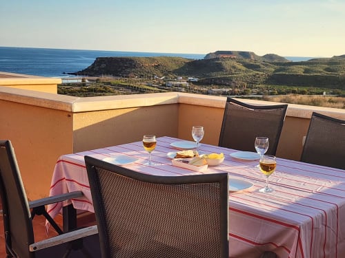 Terraza en la azotea de BAKIT HOUSE Águilas con vistas al mar, mesa de comedor, copas de vino y colinas costeras
